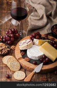 Glass of red wine with selection of various cheese on the board and grapes on wooden table background. Blue Stilton, Red Leicester and Brie Cheese and knife with linen kitchen cloth.
