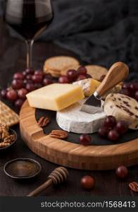 Glass of red wine with selection of various cheese on the board and grapes on wooden table background. Blue Stilton, Red Leicester and Brie Cheese and knife with honey.