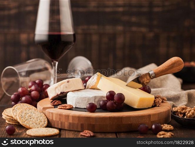 Glass of red wine with selection of various cheese on the board and grapes on wooden table background. Blue Stilton, Red Leicester and Brie Cheese and knife.