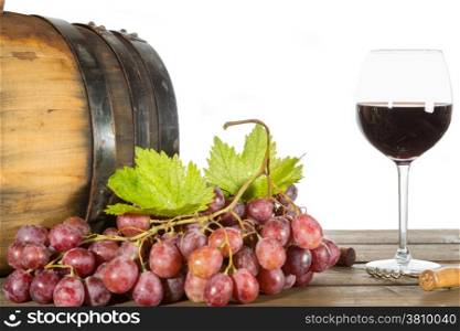 Glass of red wine with some grapes and oak barrels
