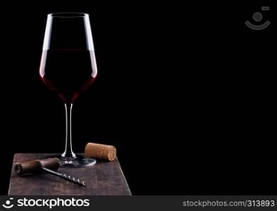 Glass of red wine with vintage corkscrew opener and cork on wooden board on black