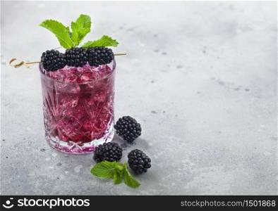 Glass of refreshing summer cocktail with blackberry, ice and mint on light table background. Soda and alcohol mix. Space for text