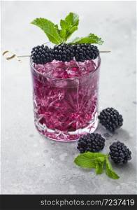 Glass of refreshing summer cocktail with blackberry, ice and mint on light table background. Soda and alcohol mix.