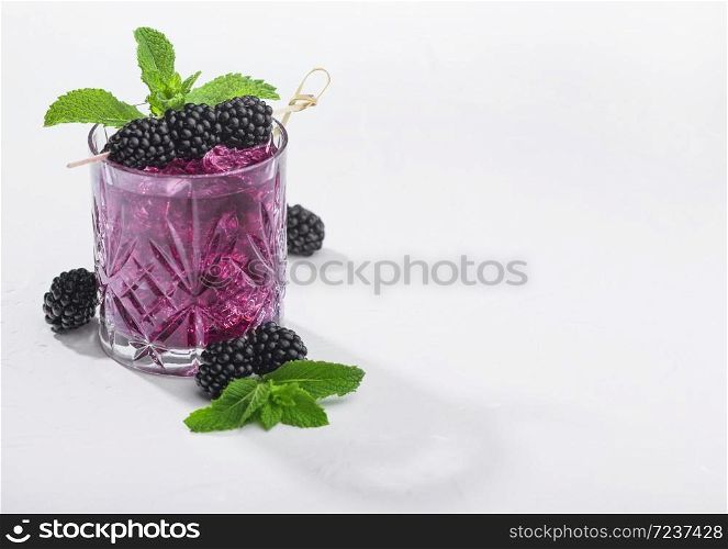 Glass of refreshing summer cocktail with blackberry, ice and mint on white background. Soda and alcohol mix. Hard light with deep shadow.