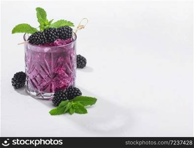 Glass of refreshing summer cocktail with blackberry, ice and mint on white background. Soda and alcohol mix. Hard light with deep shadow.