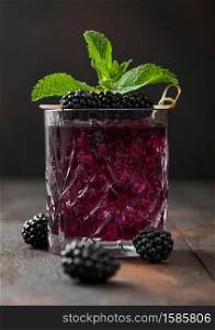 Glass of refreshing summer cocktail with blackberry, ice and mint on wooden background with raw berries. Soda and alcohol mix.