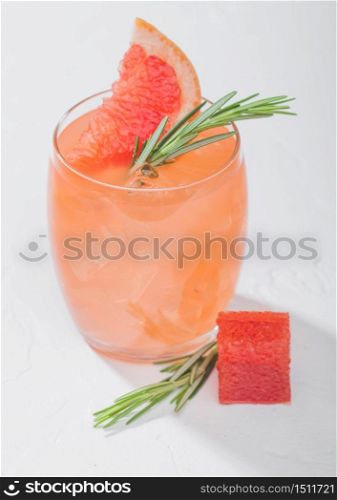 Glass of refreshing summer red grapefruit cocktail with square fruit slice and rosemary on white background. Macro