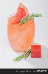 Glass of refreshing summer red grapefruit cocktail with square fruit slice and rosemary on white background. Macro