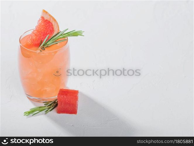 Glass of refreshing summer red grapefruit cocktail with square fruit slice and rosemary on white background. Space for text