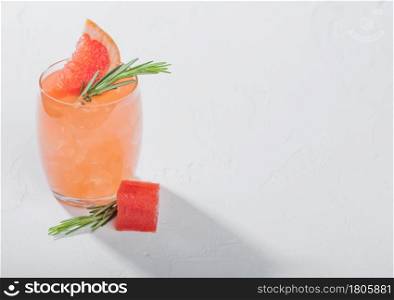 Glass of refreshing summer red grapefruit cocktail with square fruit slice and rosemary on white background. Space for text