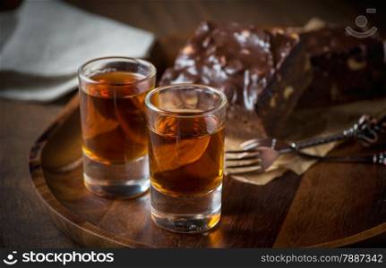 Glass of rum on wooden tray with chocolate brownies in the background, selective focus