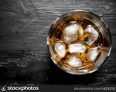 glass of rum with ice. On a black wooden background.. glass of rum with ice.