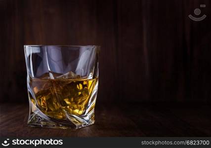 Glass of scotch whiskey and ice on a wooden background with copyspace