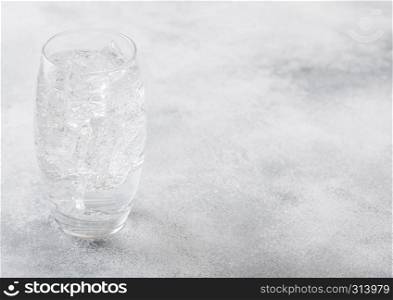 Glass of sparkling water lemonade drink with ice cubes and bubbles on stone kitchen background.
