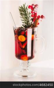 Glass of spiced mulled wine with berries and fir branch on light background