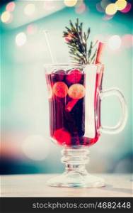 Glass of spiced mulled wine with berries and fir branch on table at bokeh lighting background, retro toned