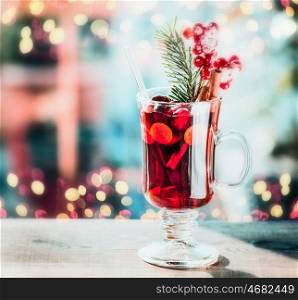 Glass of spiced mulled wine with berries and fir branch on table at festive bokeh lighting background
