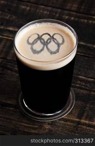 Glass of stout beer top with olympics shape on wooden background