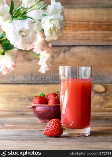 Glass of strawberry juice with fresh strawberries on the wooden background