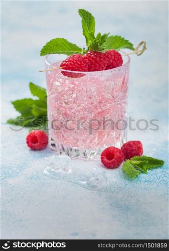 Glass of summer pink lemonade cocktail with raspberries, ice and mint on blue background. Space for text
