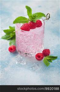 Glass of summer pink lemonade cocktail with raspberries, ice and mint on blue background. Space for text
