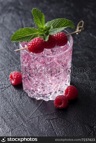 Glass of summer pink lemonade cocktail with raspberries, mint and ice cubes on black background. Space for text