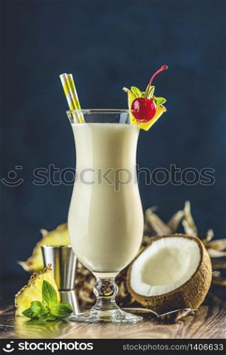 Glass of tasty Frozen Pina Colada Traditional Caribbean cocktail decorated by slice of pineapple and cherry, served on dark wooden background.