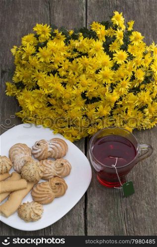 glass of tea, bouquet of yellow flowers and plate with cookies, a still life on a wooden table, a subject food and drinks