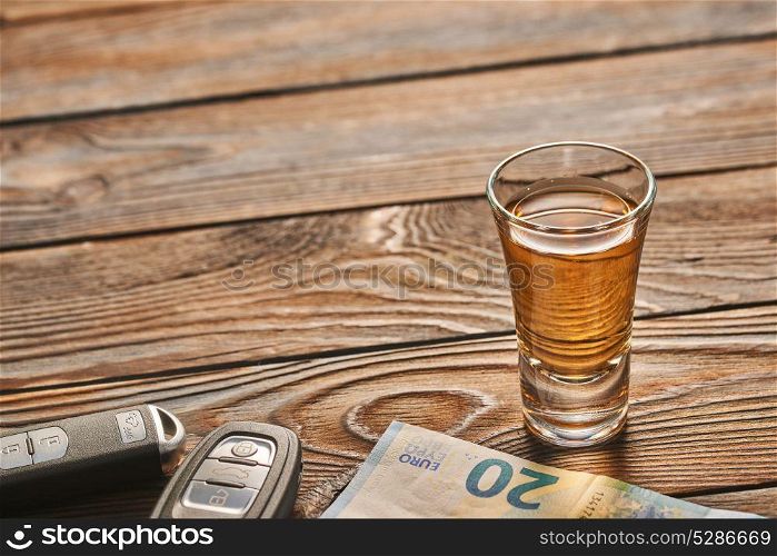 Glass of tequila or alcohol drink and car key on rustic wooden table with copy-space. Drink and drive and alcoholism concept. Safe and responsible driving concept.