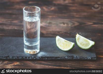 Glass of tequila with lime wedges on the stone board