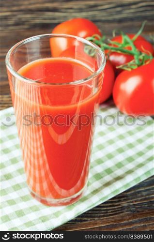 Glass of tomato juice and fresh red tomatoes on brown wooden table. tomato juice in glass and fresh tomatoes on wooden table