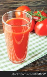 Glass of tomato juice and fresh red tomatoes on brown wooden table. tomato juice in glass and fresh tomatoes on wooden table