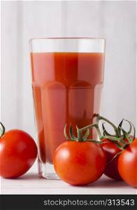 Glass of tomato juice with fresh raw tomatoes on wooden background