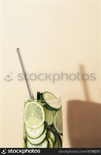 Glass of tonic water with cucumber and lime and metal straw on yellow background. Summer cocktail close-up. Healthy drinking. Sparkling water beverage