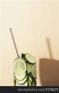 Glass of tonic water with cucumber and lime and metal straw on yellow background. Summer cocktail close-up. Healthy drinking. Sparkling water beverage