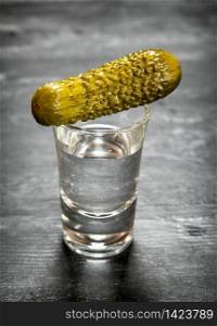 Glass of vodka with pickled gherkins. On a black wooden background.. Glass of vodka with pickled gherkins.