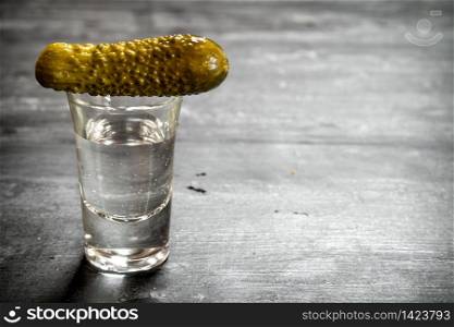 Glass of vodka with pickled gherkins. On a black wooden background.. Glass of vodka with pickled gherkins.