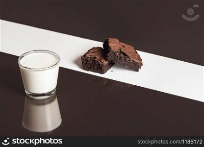 Glass of warm milk and two pieces of brownies on a white and brown background. Duotone image of unhealthy breakfast. Chocolate cake and milk.