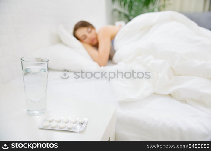 Glass of water and pack of pills on table and woman sleeping in background