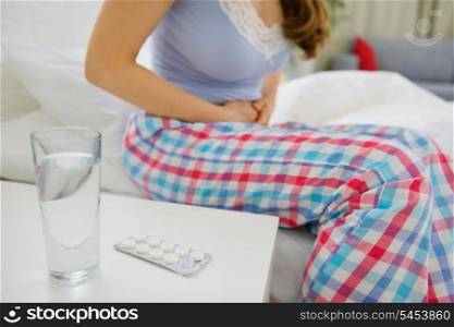 Glass of water and pills on table and woman with abdominal ache in background