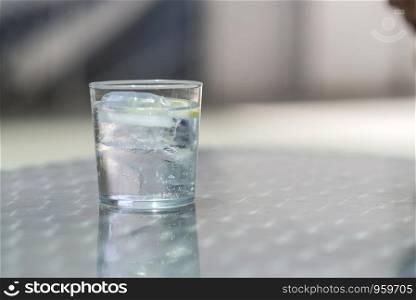 Glass of water with ice on a metallic table outdoors in a bright day