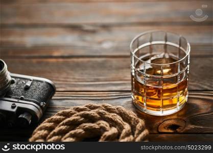 Glass of whiskey and vintage old 35mm rangefinder camera on wooden background