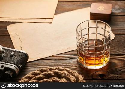 Glass of whiskey and vintage old 35mm rangefinder camera on wooden background with antique XIX century map