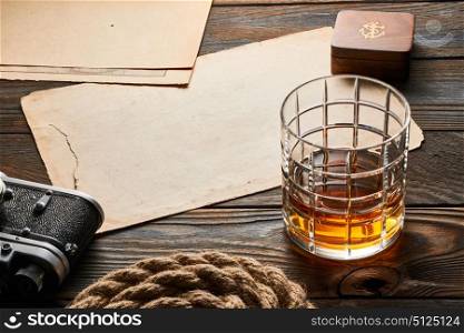 Glass of whiskey and vintage old 35mm rangefinder camera on wooden background with antique XIX century map