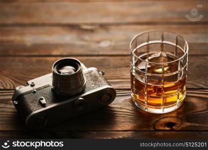 Glass of whiskey and vintage old 35mm rangefinder camera on wooden background