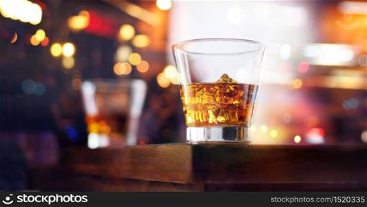 Glass of whiskey drink with ice cube on table wooden bar background