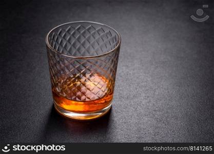 Glass of whiskey on a black stone table. Top view with copy space. A glass of whiskey or cognac on a black concrete table. Relaxation time