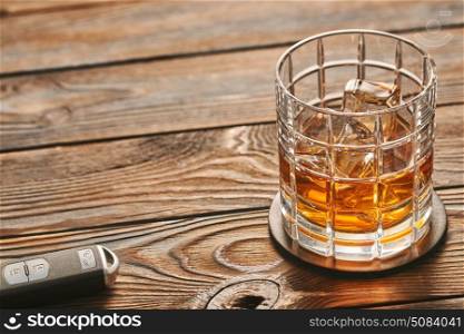 Glass of whiskey or alcohol drink with ice cubes and car key. Drink and drive concept. . Glass of whiskey or alcohol drink with ice cubes and car key on rustic wooden table with copy-space. Drink and drive and alcoholism concept. Safe and responsible driving concept.