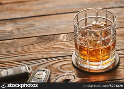 Glass of whiskey or alcohol drink with ice cubes and car key on rustic wooden table with copy-space. Drink and drive and alcoholism concept. Safe and responsible driving concept.