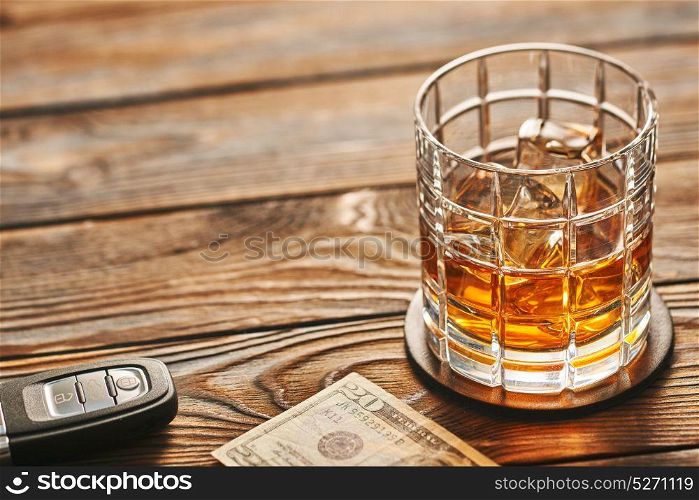 Glass of whiskey or alcohol drink with ice cubes and car key on rustic wooden table with copy-space. Drink and drive and alcoholism concept. Safe and responsible driving concept.
